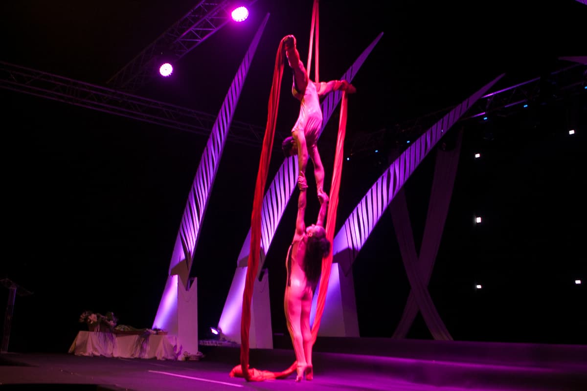 Dúo de acrobacia aérea en telas rojas sobre un escenario con iluminación púrpura