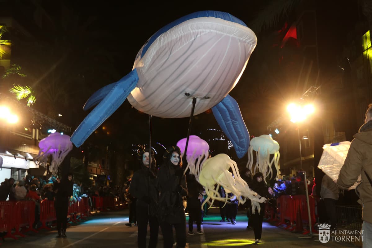Ballena hinchable gigante flotando sobre un cortejo nocturno con medusas luminosas
