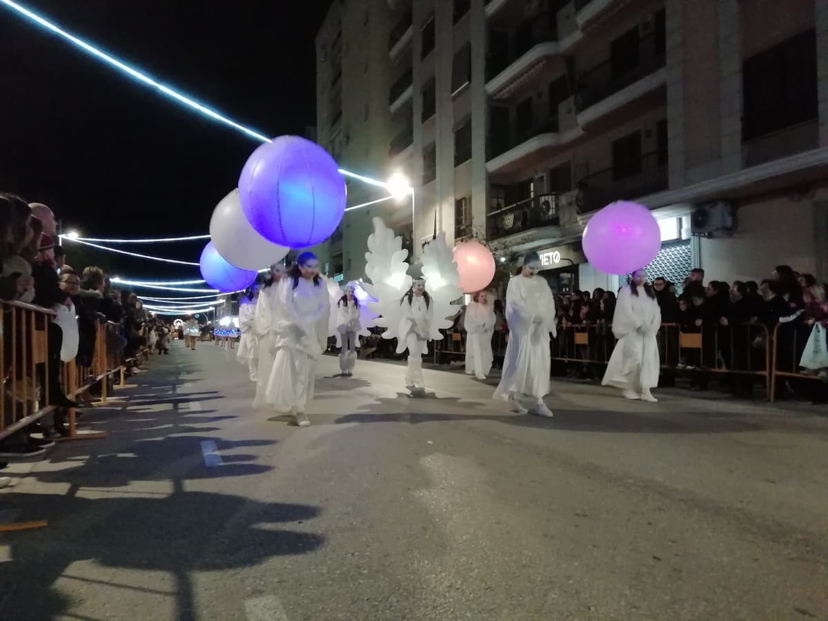 Artistas con túnica blanca portando esferas de luz en un pasacalles nocturno
