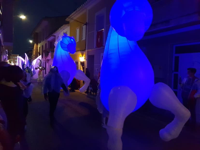 Dos caballos hinchables iluminados en azul en cabalgata nocturna por calle estrecha