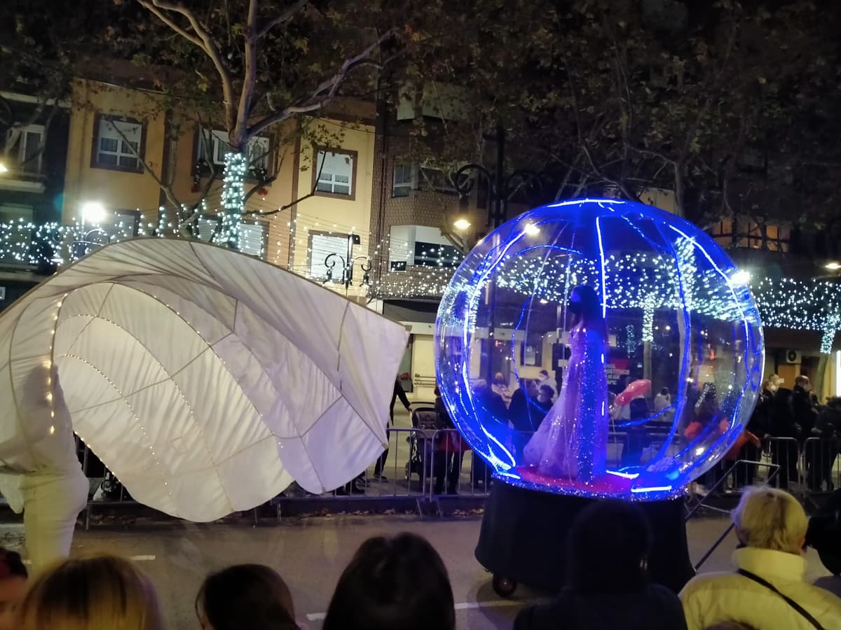 Esfera azul iluminada junto a un elemento en forma de concha en una calle con luces de Navidad