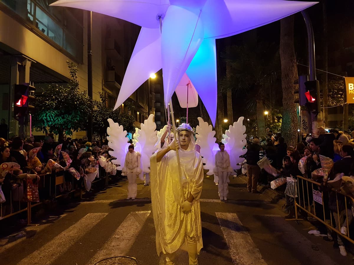 Estrella de Oriente iluminada junto a figuras aladas y un personaje con túnica dorada en una cabalgata