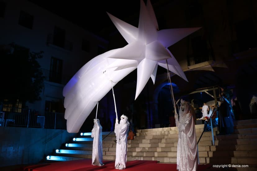 Estrella con cola de cometa iluminada sobre figuras con túnica blanca en una escalinata