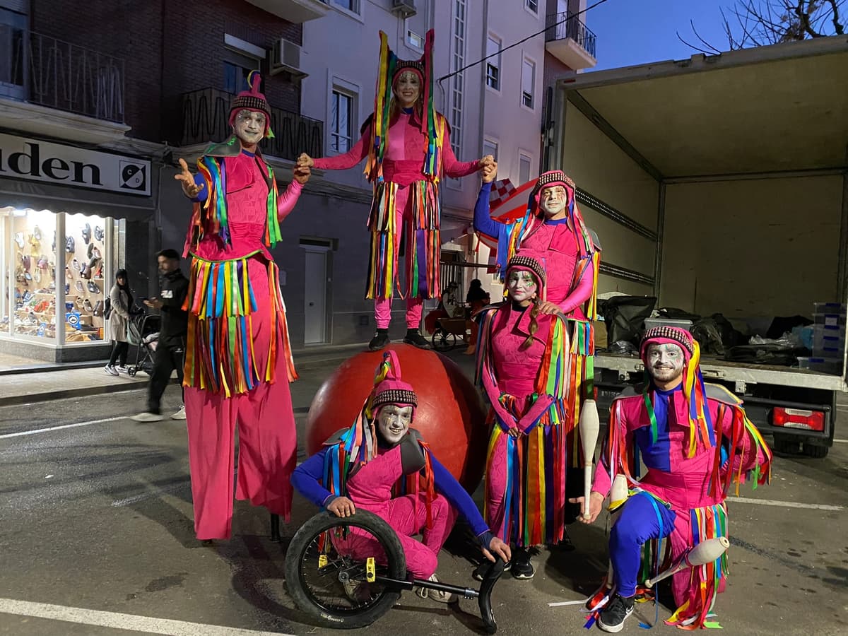 Zancudos con vestuario circense y unicornio en calle durante el día, junto a artista en monociclo
