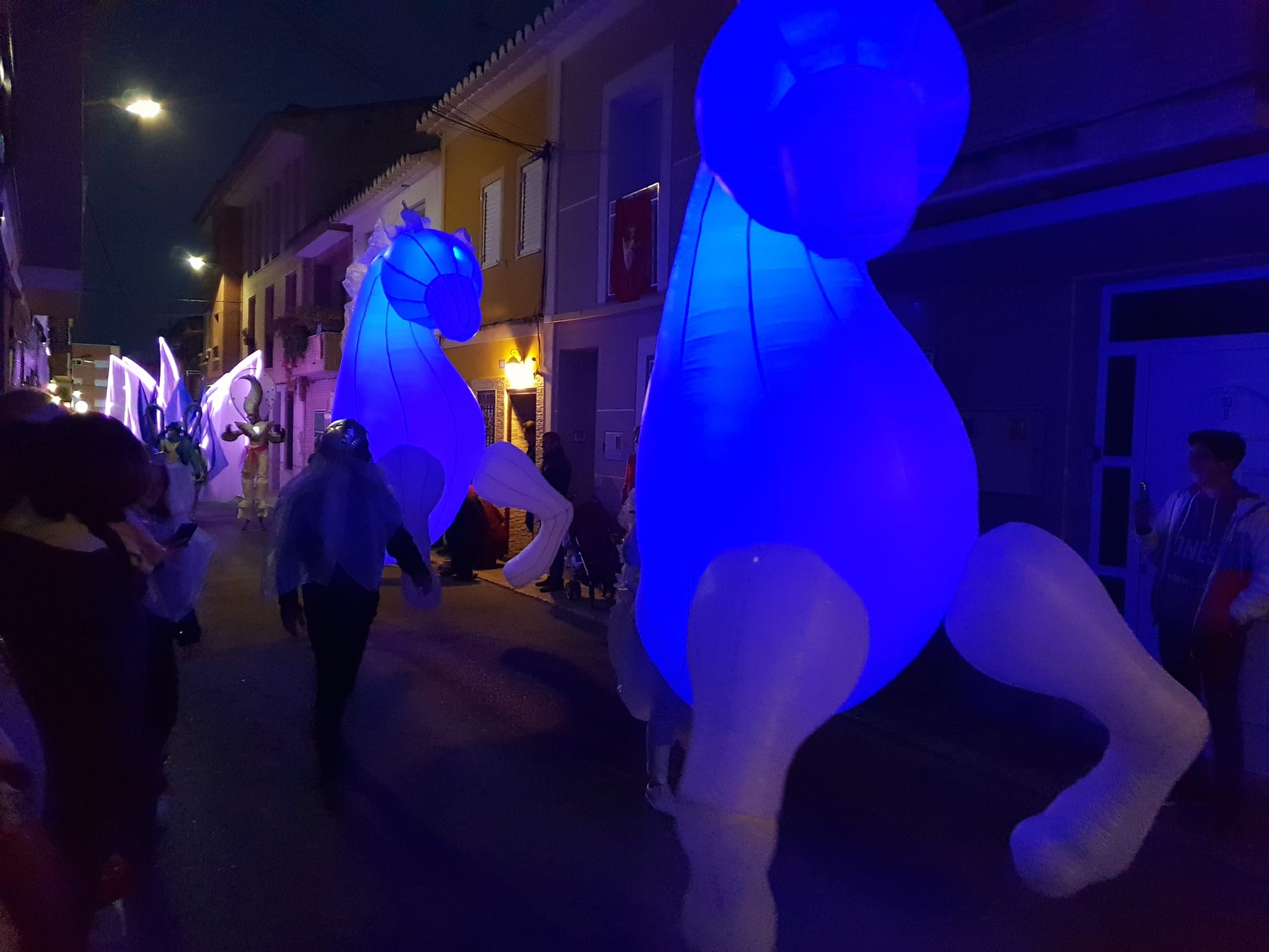 Dos caballos hinchables iluminados en azul en cabalgata nocturna por calle estrecha