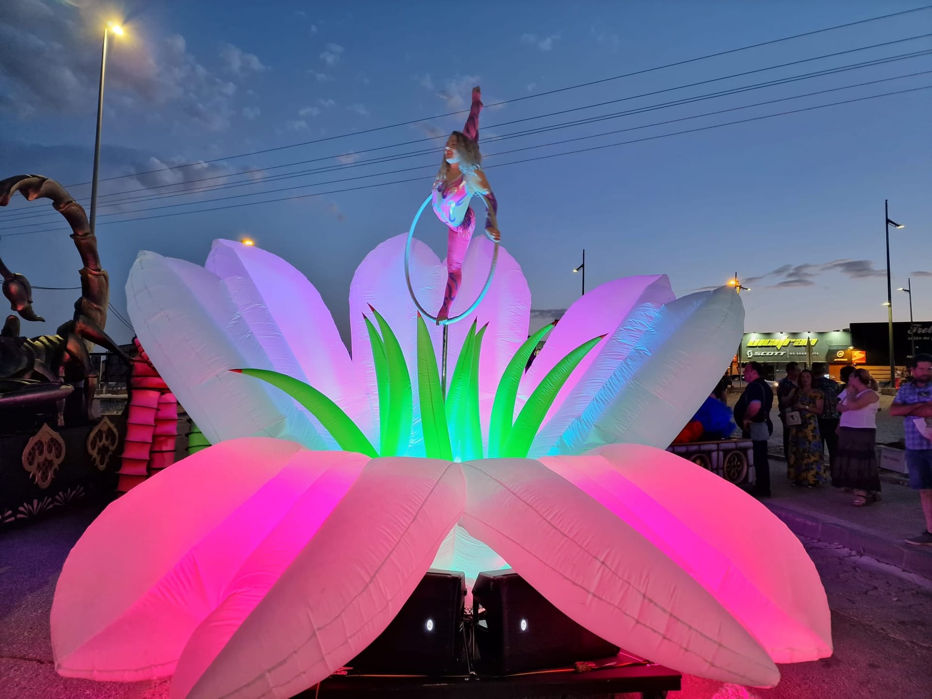 Carroza flor hinchable gigante iluminada con acróbata en aro al atardecer