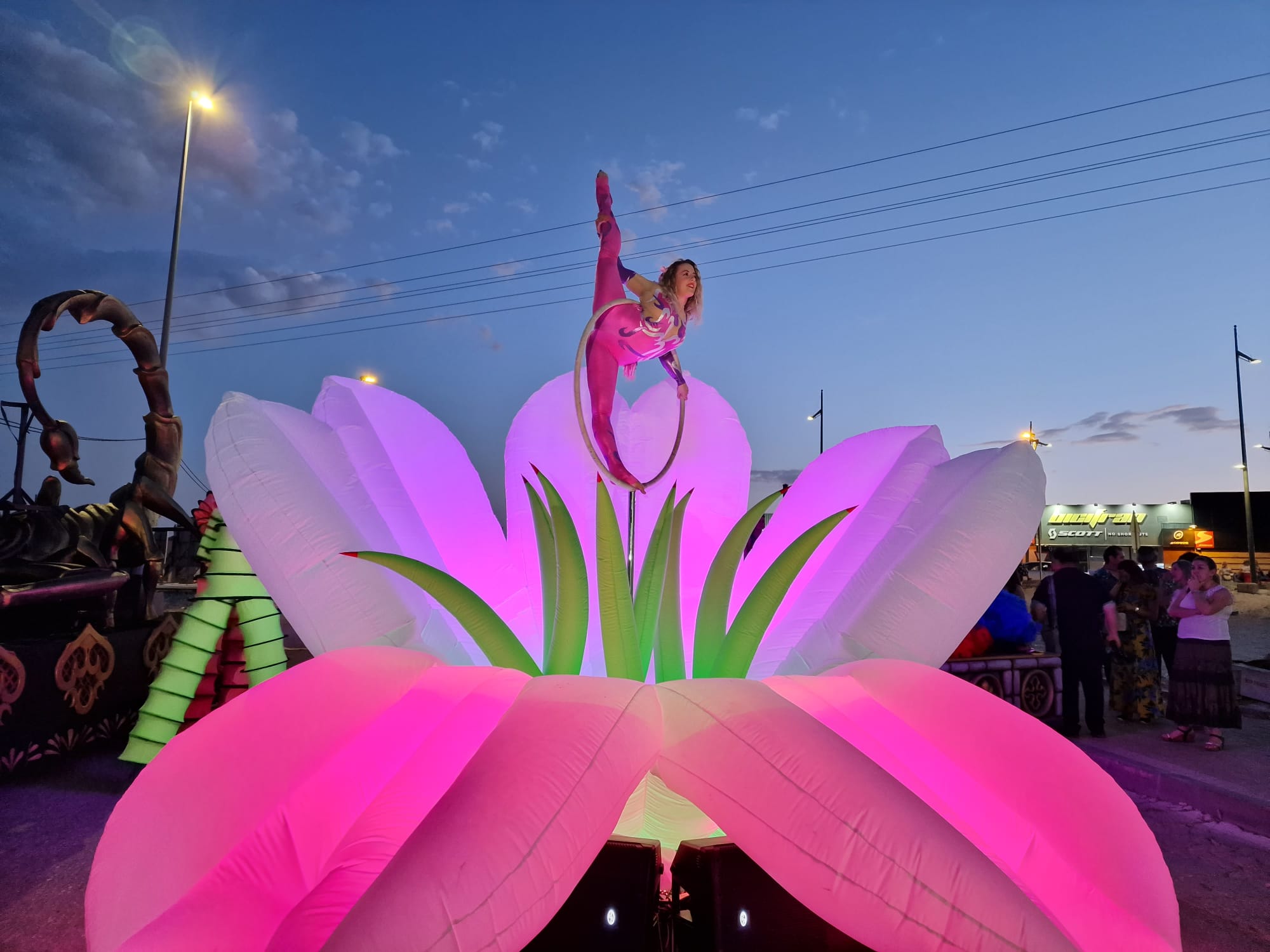 Acróbata en aro sobre carroza flor hinchable gigante iluminada al atardecer